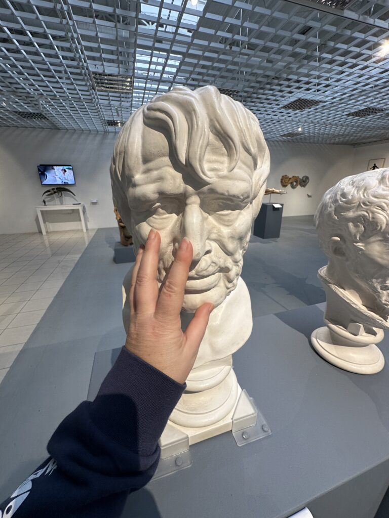 Slika prikazuje roko, ki s tipom raziskuje kip v taktilni galeriji.